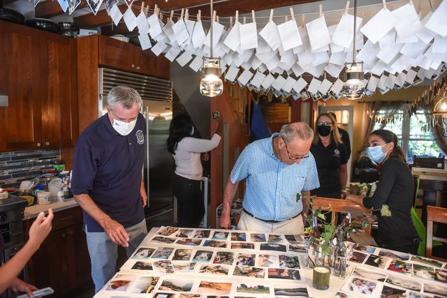 Photographs are pinned on clotheslines to dry out, with Mayor de Blasio and Senator Schumer looking at the ones drying out on a table